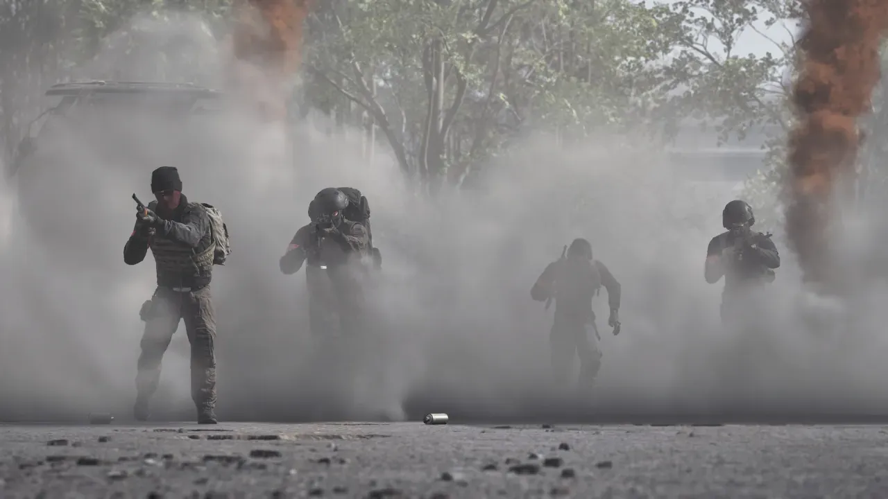 Four soldiers advance through white and orange smoke across open pavement.
